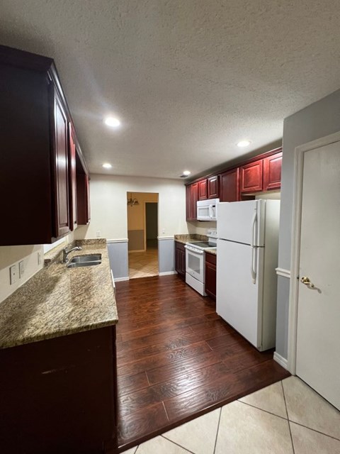A kitchen with dark brown cabinets and a granite counter.