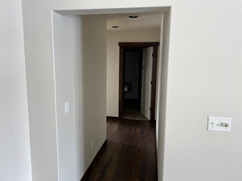 a hallway with white walls and wood floors and a door to a bathroom