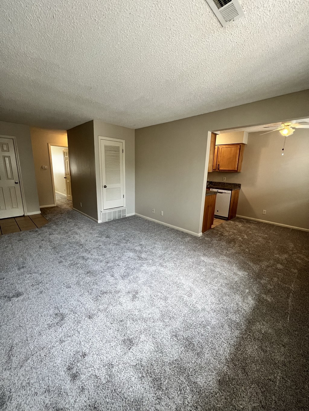an empty living room with carpet and a kitchen