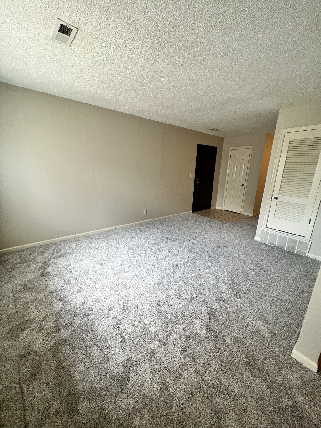 an empty living room with carpeting and a door to a bedroom