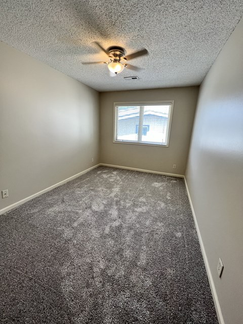 an empty bedroom with a ceiling fan and a window