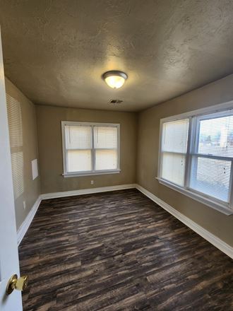 an empty room with wood floors and two windows