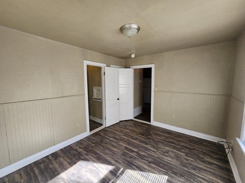 a empty living room with wood floors and a door to a kitchen