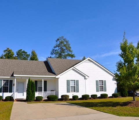 A white house with green shutters and a grey roof.