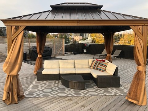 A wooden gazebo with a white couch and a black table in front of it.