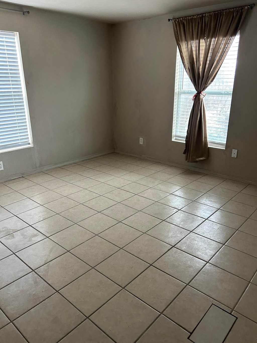 an empty living room with tiled flooring and two windows