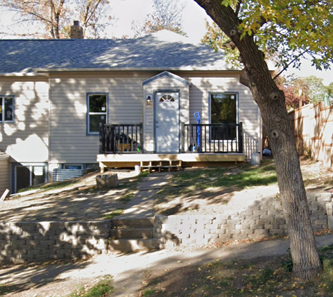 the front of the house with a deck and a tree