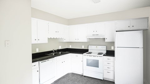A white kitchen with black countertops and white appliances.