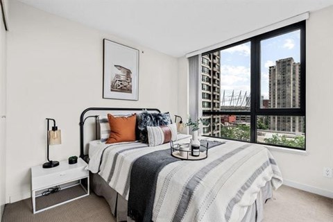 A bedroom with a large bed and a view of a city skyline through the window.