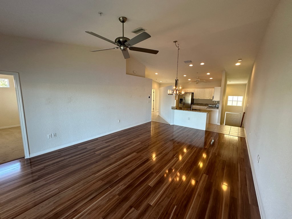 an empty living room with wooden floors and a ceiling fan
