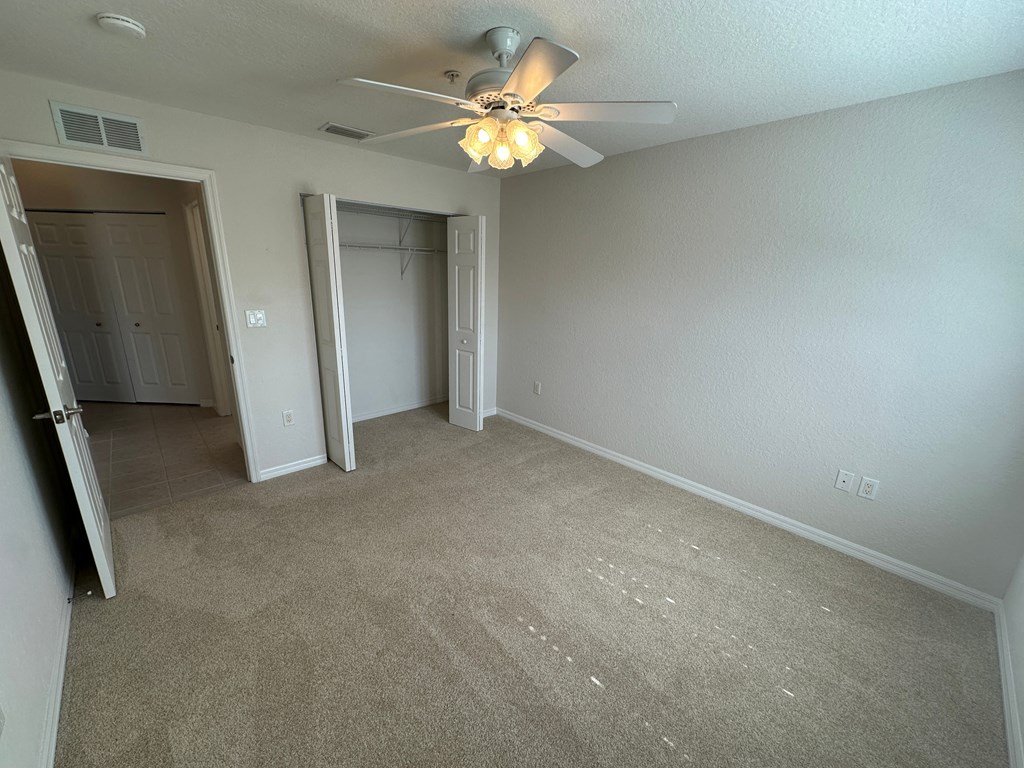 an empty living room with a ceiling fan and a closet