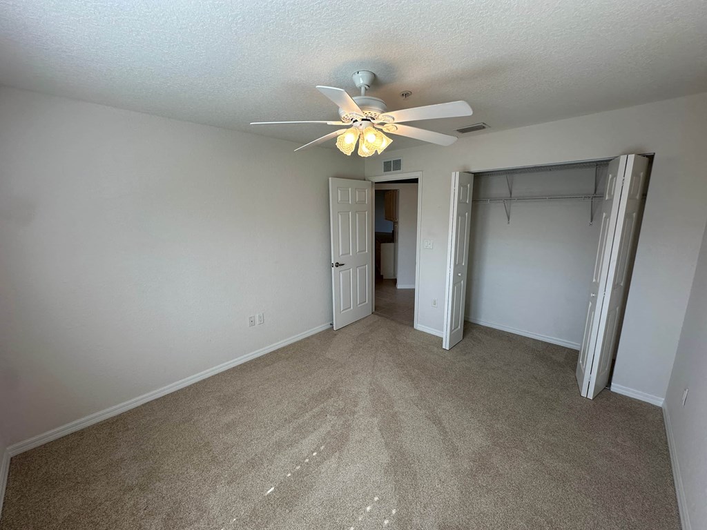 an empty living room with a ceiling fan and a closet