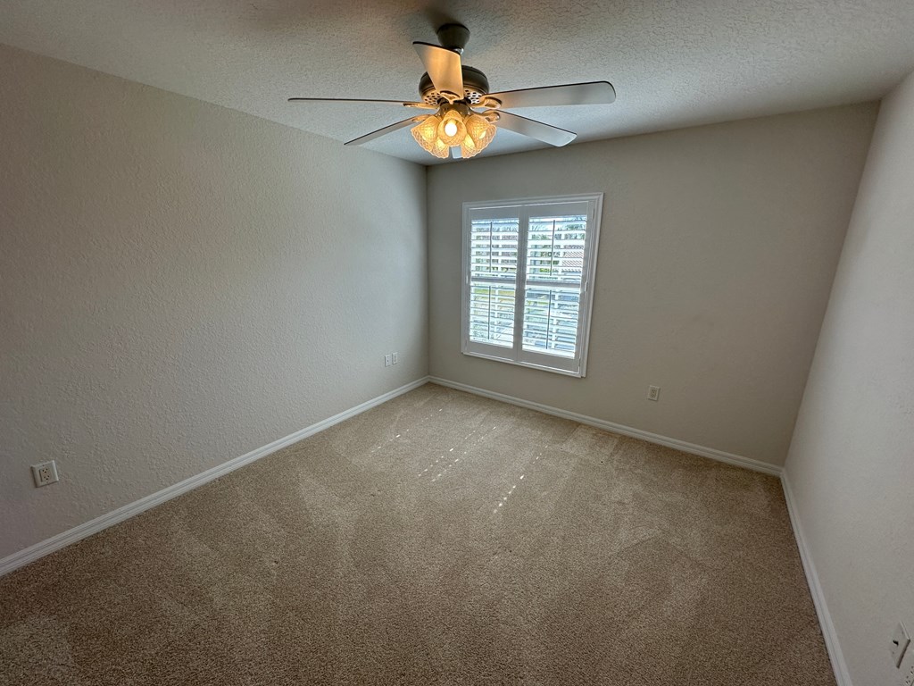 an empty bedroom with a ceiling fan and a window