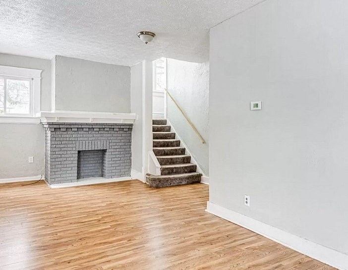 an empty living room with a brick fireplace and wooden floors