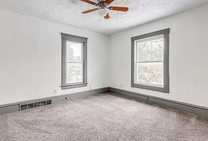 an empty room with a ceiling fan and two windows