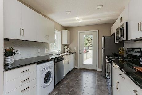 A modern kitchen with white cabinets and black countertops.