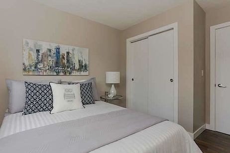 A bedroom with a bed, two pillows, a nightstand with a lamp, and a painting on the wall.