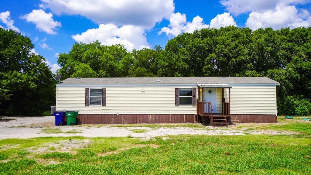 A small house with a brown roof and a white door is surrounded by greenery.