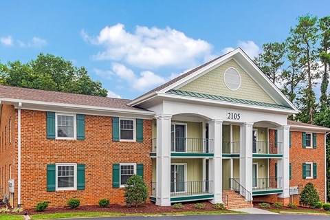 A red brick building with green shutters and a white porch.
