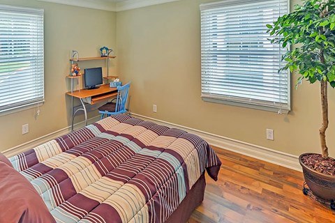 A bedroom with a bed, desk, chair, and a potted plant.