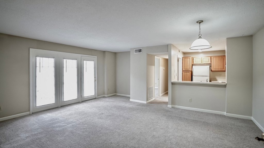 an empty living room with large windows and a kitchen