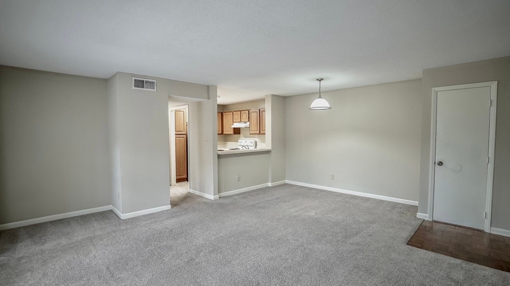 an empty living room with a kitchen in the background