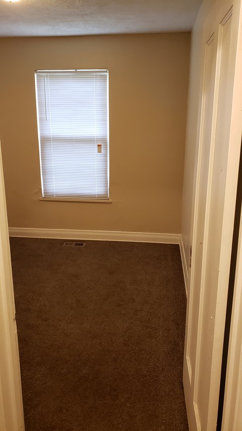 A room with a carpeted floor and a window with blinds.