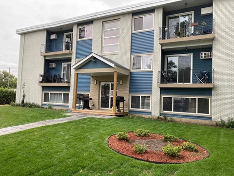 the front of an apartment building with a circle of landscaping in the grass