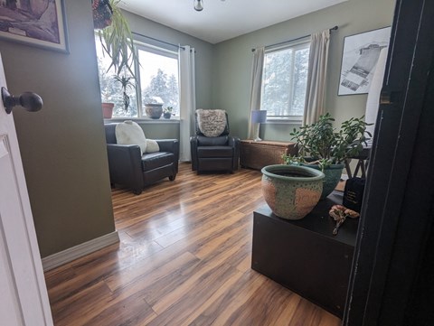a living room with a hard wood floor and chairs and plants