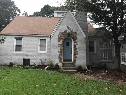 A house with a grey facade and a stone arched doorway.