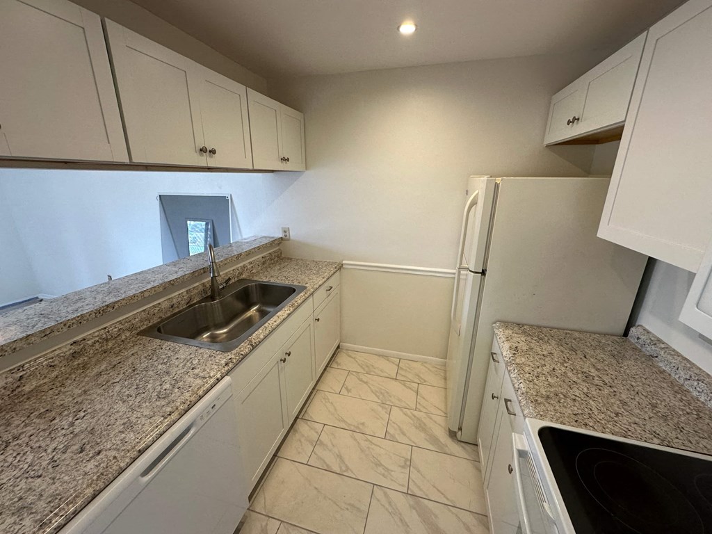 an empty kitchen with granite counter tops and white cabinets