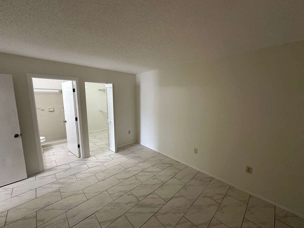 an empty living room with a tiled floor and a door to a bathroom
