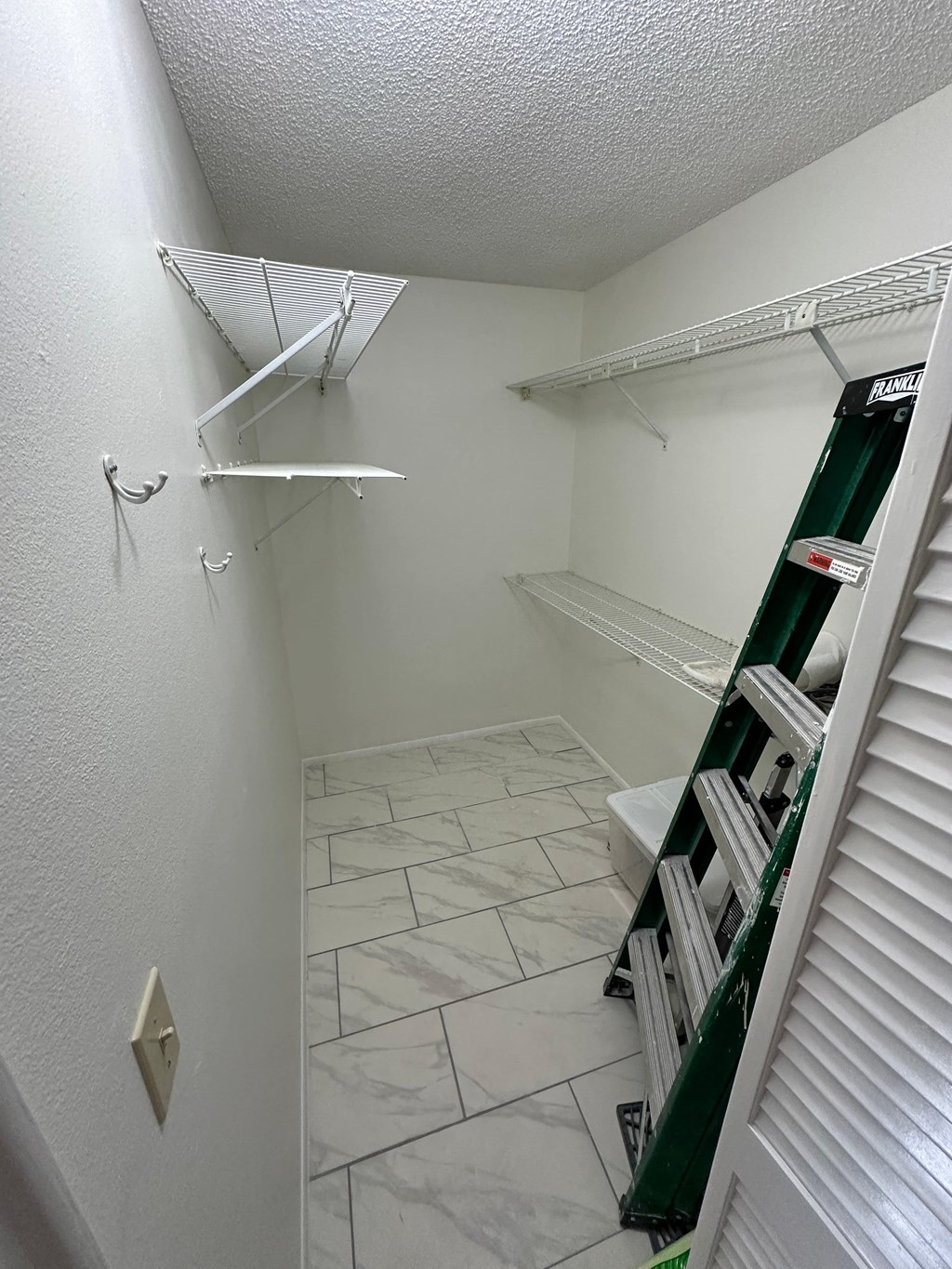 a walk in closet in a bathroom with white walls and white tile floor and white