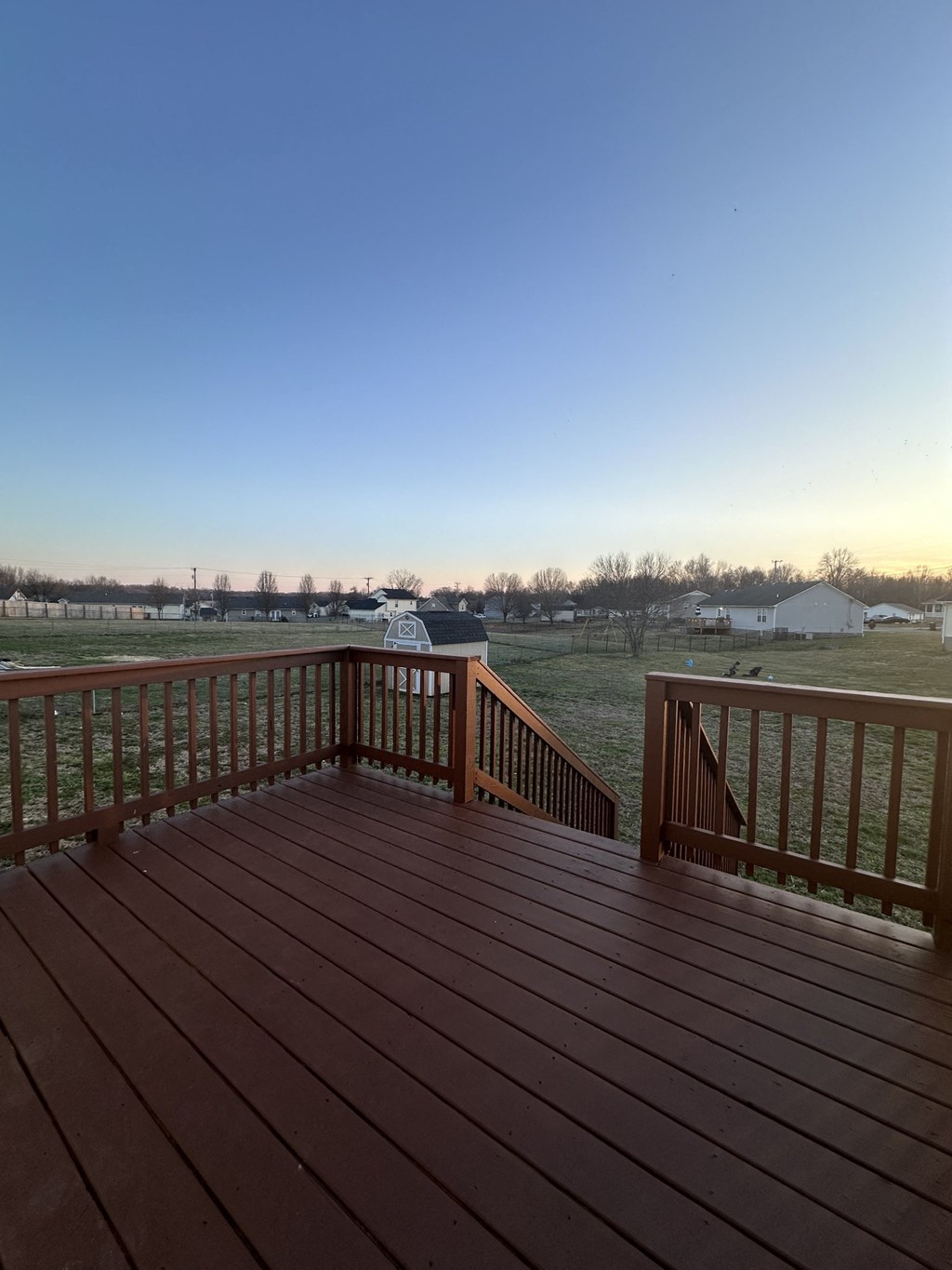 A wooden deck with a view of a field and houses.