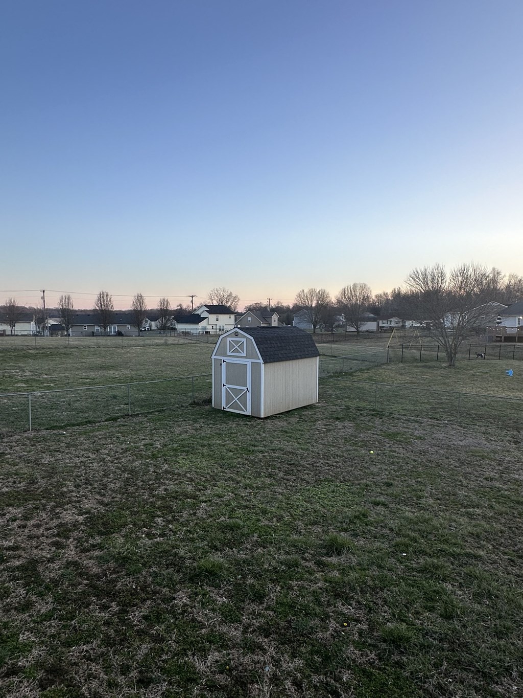 A small white shed sits in the middle of a grassy field.