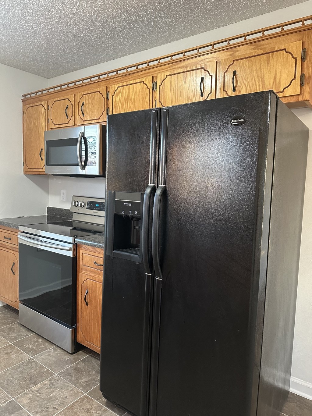 A black refrigerator stands in a kitchen with wooden cabinets.