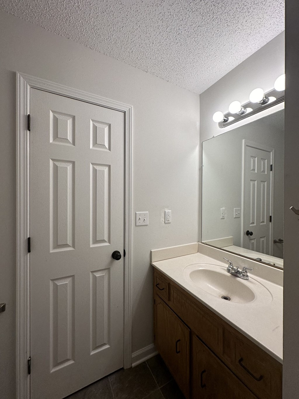 A white door is in a bathroom with a mirror and lights above it.