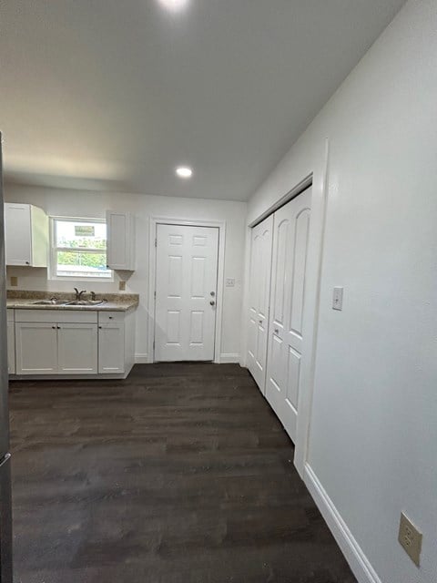 a kitchen with white cabinets and white walls and a wood floor