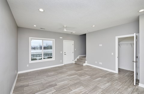 A spacious room with a large window, hardwood flooring, and a ceiling fan.