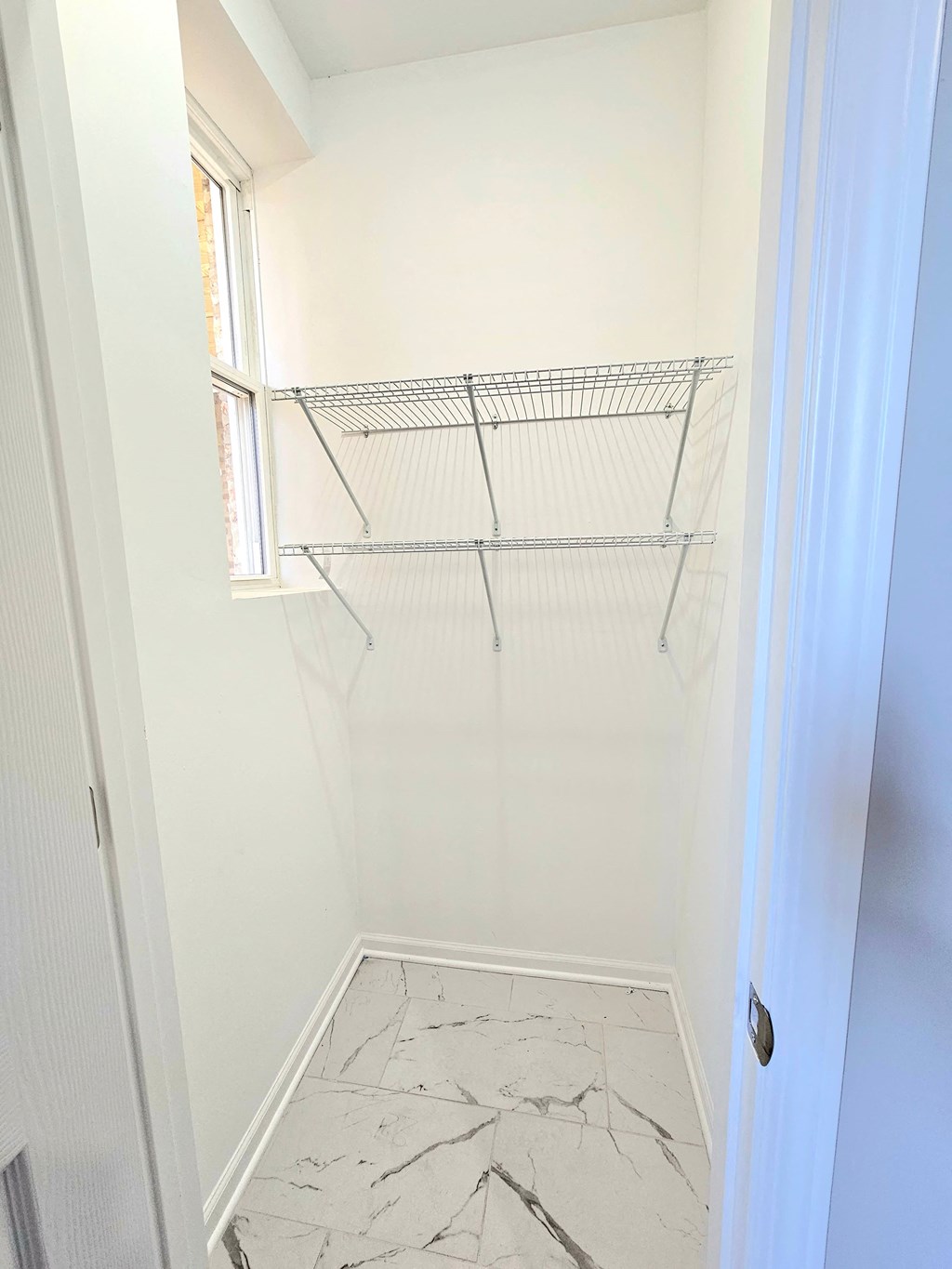 a large white closet with a window and a white marble floor