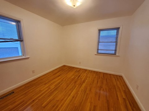 a bedroom with a hard wood floor and two windows
