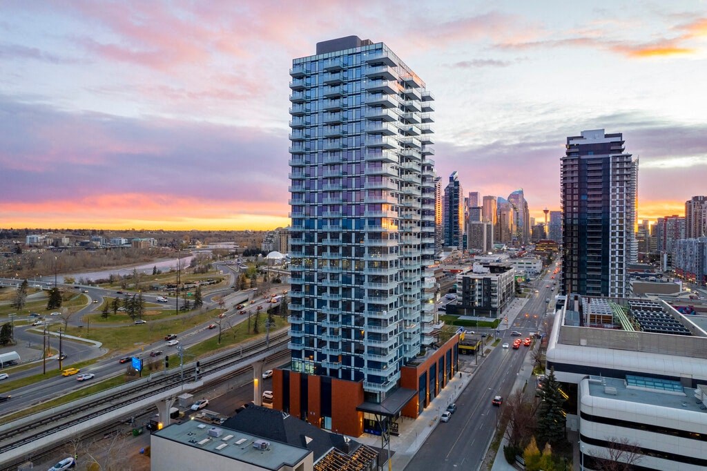 A tall, modern building stands in the foreground of a cityscape at sunset.