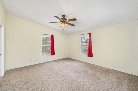 an empty living room with a ceiling fan and red curtains