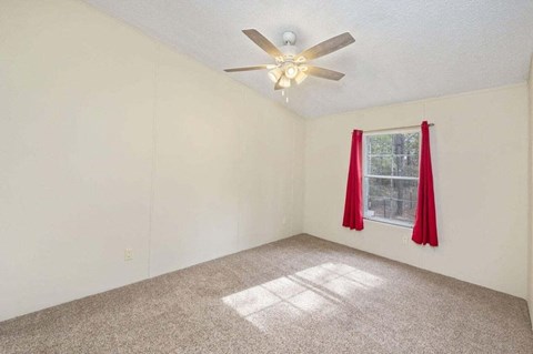 an empty bedroom with a ceiling fan and red curtains