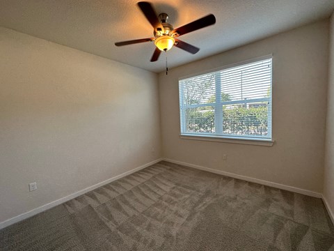 an empty bedroom with a ceiling fan and a window