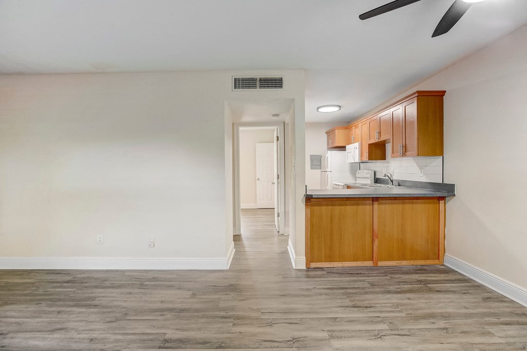 the living room and kitchen of an apartment with wood flooring and white walls