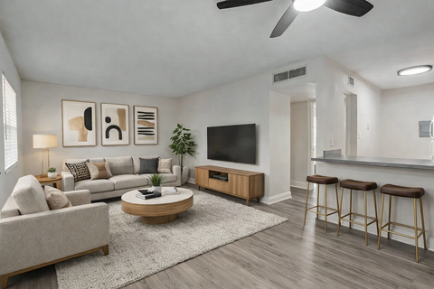A living room with a grey couch, a coffee table, a television, and a bar area.
