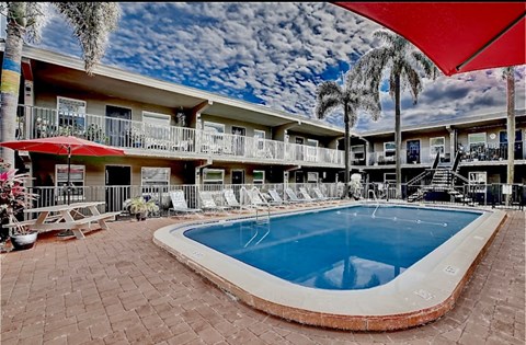 A pool surrounded by a red umbrella and chairs.