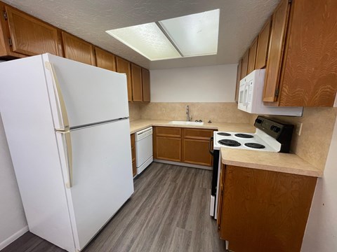 A white refrigerator stands in a kitchen with wooden cabinets and a stove.