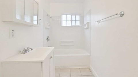 A white bathroom with a sink, mirror, and bathtub.